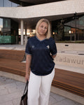 Woman wearing a navy blue shirt with a Bosnian lily, standing in front of a modern building.